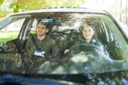Happy male instructor and teen girl smiling during her first driving lesson inside a car. Female...