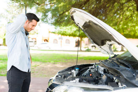 Stressed male driver looking at his car engine with the hood open. Attractive young man having...