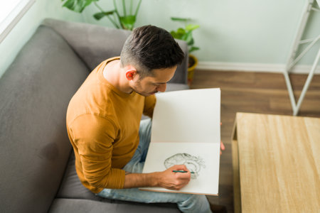 Top view of a handsome man in his 30s sketching with a pencil on a notebook. Latin man with a drawing hobby during a leisure dayの写真素材