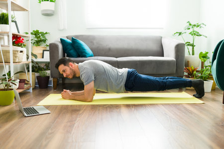 Sporty man in his 30s strenghtening his abdomen and body with a forearm plank while working out in...