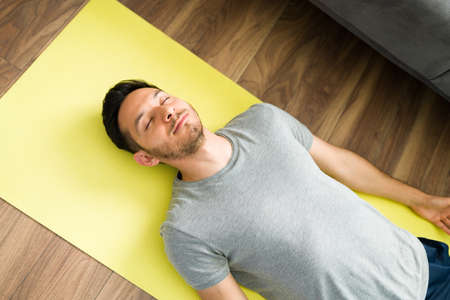 Top view of a good-looking man lying in a yoga mat with his eyes closed. Latin man in his 30s doing a corpse pose and relaxingの写真素材