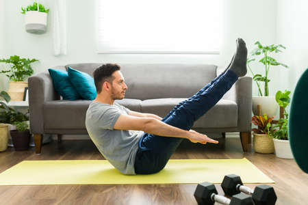 Side view of a fit young man training with a cardio routine in the living room. Adult fit man doing...