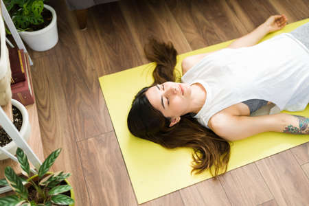 Top view of a fit attractive woman lying in a yoga mat with her eyes closed. Hispanic woman doing a corpse pose and relaxingの写真素材