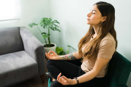 Young woman doing activities to improve her mental health. Positive woman sitting in an easy yoga...