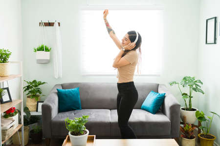 Attractive woman dancing while feeling happy and free during a relaxed day at home. Latin woman listening to music and her favorite song with headphonesの写真素材