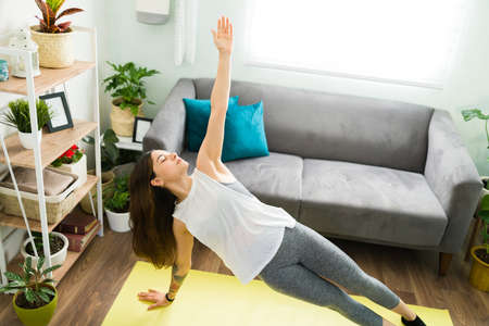 Pretty young woman exercising and relaxing while doing a yoga workout. Active woman in a side plank...