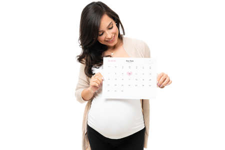 Cheerful pregnant woman showing a calendar with her marked due date. Beautiful pregnant woman planning for the birth of her babyの写真素材