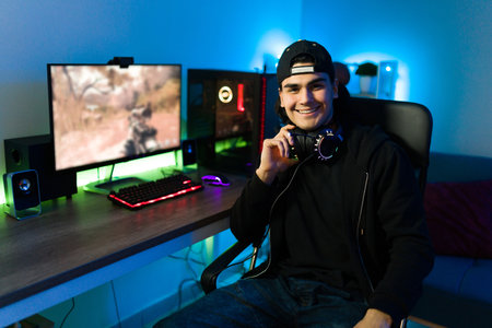 Handsome man sitting in front of his gaming computer with led lights at his bedroom. Young gamer...