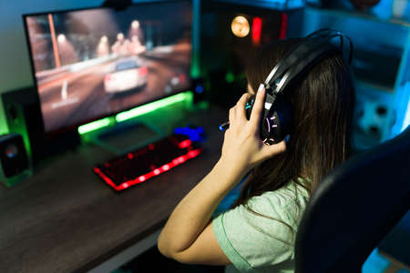Rear view of a female woman gamer with headphones preparing to play an online video game in a gaming computer PC with led lightsの写真素材