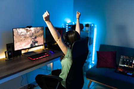 Happy and excited female gamer celebrating in front of her gaming computer because of her victory win in an online video gameの写真素材