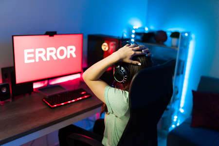 Shocked female gamer with her hands on the head and looking at the computer screen with an error message. Young woman having a glitch on her online video gameの写真素材