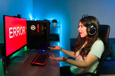 Upset caucasian female gamer looking at the error message on the computer screen while playing an online video game in her bedroomの写真素材