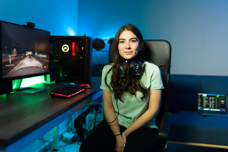 Attractive young woman sitting at her desk with a gaming computer and taking a break from playing a video game. Female gamer smiling and having funの写真素材
