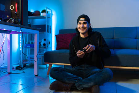 Excited young man smiling and playing an action video game with a remote controller in the floor of her bedroomの写真素材
