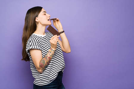 Profile of an attractive young woman eating a big chocolate candy bar. Beautiful woman with sugar cravings enjoying a chocolateの写真素材