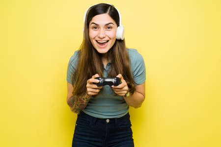 Excited latin young woman with headphones screaming in excitement and enjoying an online video game while using a remote controllerの写真素材