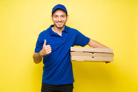 Happy delivery man smiling and carrying big boxes of pizza while doing a thumbs up. Handsome male...