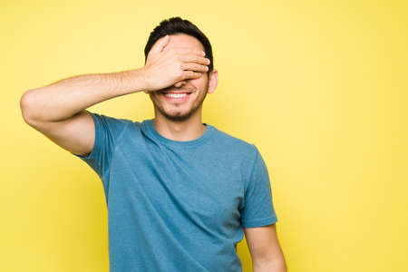 Happy and cheerful man smiling and waiting for a surprise gift. Latin handsome man feeling excited and laughing while covering his eyesの写真素材