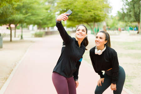 Gorgeous hispanic woman in activewear smiling and taking a selfie with her fit best friend in the...