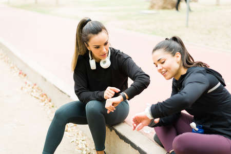 Beautiful young woman pointing to her smartwatch and setting the stopwatch. Women best friends with...