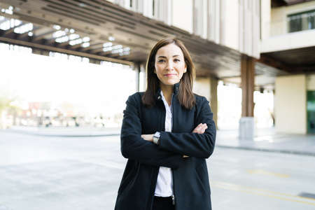 Smart businesswoman making eye contact and smiling while standing outside her office in a modern building in the cityの写真素材