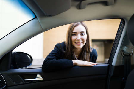 Portrait of a beautiful businesswoman smiling while talking with the driver of a car or taxi outside her office building in the cityの写真素材