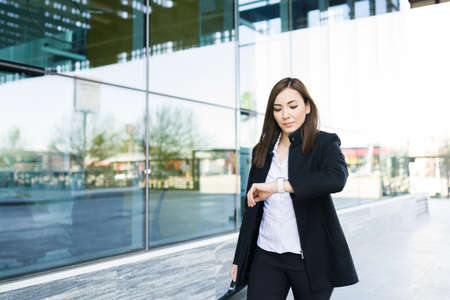 Beautiful caucasian businesswoman looking at the time in her watch and walking to a work appointment with a client in the office at a modern buildingの写真素材
