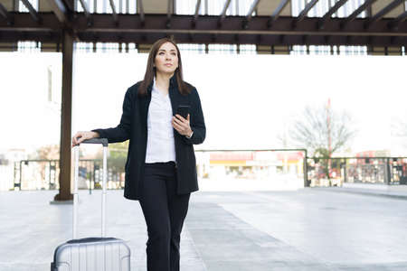 Beautiful caucasian woman waiting for a taxi cab outside the airport. Business woman with a suitcase arriving on a business trip to the cityの写真素材