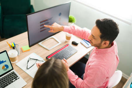 Attractive man pointing to the computer screen and business presentation while sitting at the...