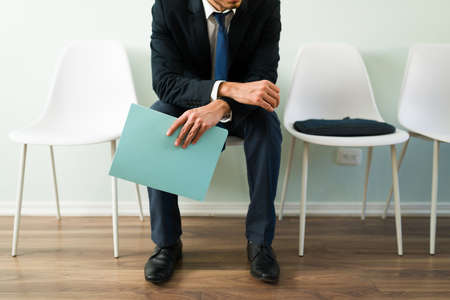 Professional man sitting at reception and holding a folder with a resume while waiting for a job interview. Businessman waiting for an appointment in a recruitment officeの写真素材