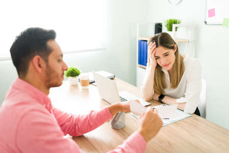 Professional male colleague sitting in the office and showing her stressed female coworker a work paper or contract where she made a mistakeの写真素材