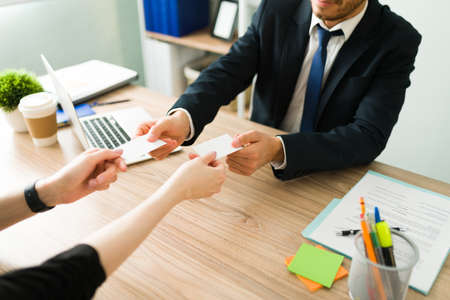 Professional hispanic man in a suit giving his business card to a caucasian female client during a meeting in a corporate officeの写真素材