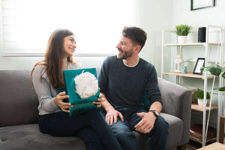 Cheerful beautiful young woman saying thanks to her handsome boyfriend or husband for her birthday anniversary present while sitting at homeの写真素材
