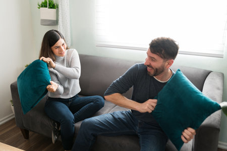 Attractive loving couple having a pillow fight while sitting on the couch. Beautiful girlfriend and...