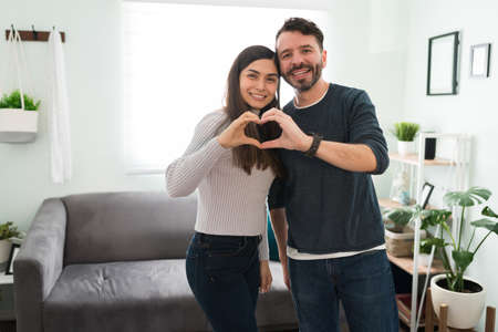 Portrait of a young couple in love putting together their hands and making a heart sign. Attractive husband and wife enjoying their time together at homeの写真素材