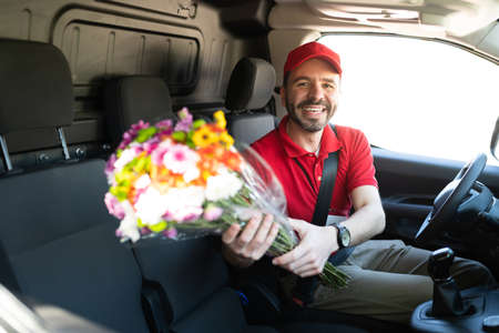 Portrait of a handsome happy man driving a delivery van from a flower shop and holding a bouquet of flowers being delivered for a home serviceの写真素材