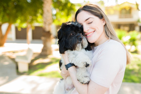 Gorgeous caucasian woman smiling and feeling happy while hugging her cute shih tzu dog. Loving dog...