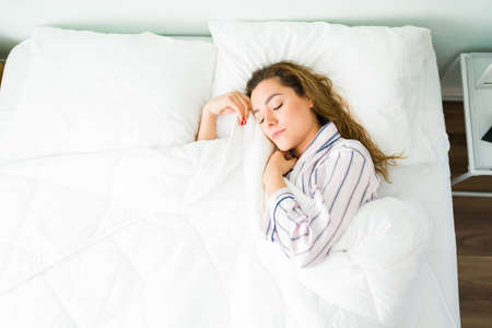 Latin woman in beautiful pajamas sleeping in a warm bed and covered with a duvet. Tired woman...