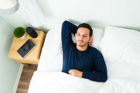 Top view of a thoughtful man resting in a comfy bed and thinking about his day after waking up in...