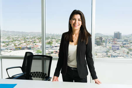 Gorgeous female boss with a beaming smile standing in front of her desk and waiting for her next...