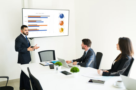 Handsome latin businessman presenting a work results and the growing business goals to his professional co-workers at the meeting roomの写真素材