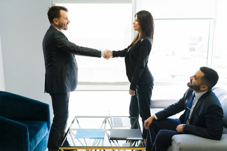 Glad to work with you. Happy businessman and businesswoman shaking hands after joining a new work team in the companyの写真素材
