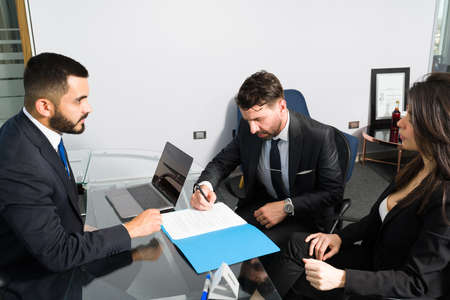 Side view of three powerful businessmen and businesswoman signing a work contract. Company representative making a business saleの写真素材