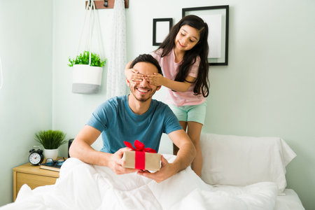 Close your eyes for a surprise. Beautiful girl giving a present to her dad for his birthday. Little daughter and young dad celebrating Father's Dayの写真素材