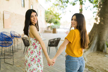 Rear view of two multiracial young women holding hands while smiling and making eye contact outdoorsの写真素材