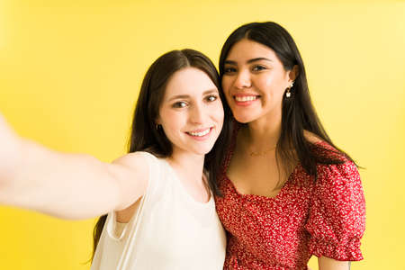 Making happy memories. Attractive caucasian woman in her 20s taking a selfie with her beautiful latin best friend against a bright colorful backgroundの写真素材