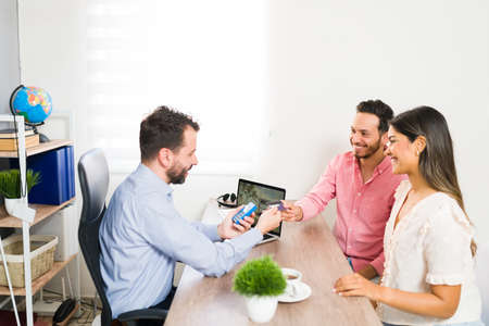 Happy young man purchasing a vacation package with a credit card. Beautiful loving couple paying for...