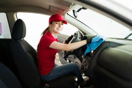 Portrait of a happy young woman smiling while cleaning the interior dashboard of a car at her work in the auto detail serviceの写真素材