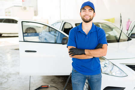 Proud of my work at the car wash. Portrait of a handsome latin young man with a cap and blue uniform working at a car wash and auto detail serviceの写真素材