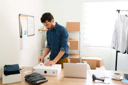 Hispanic young man in his 30 working at his startup business and putting a shipping label on a package ready to send in the mail to customersの写真素材